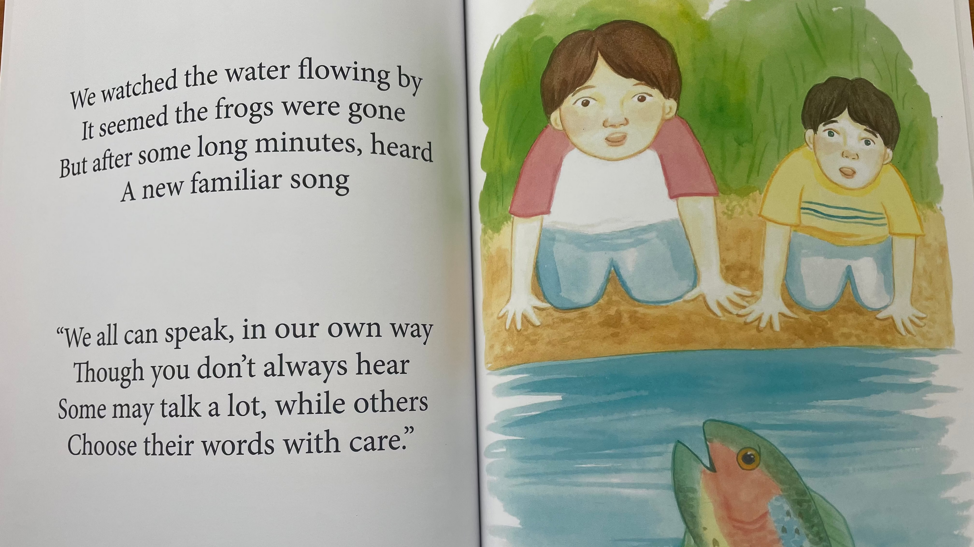 Open book with a colorful illustration of two children by a river and a fish.